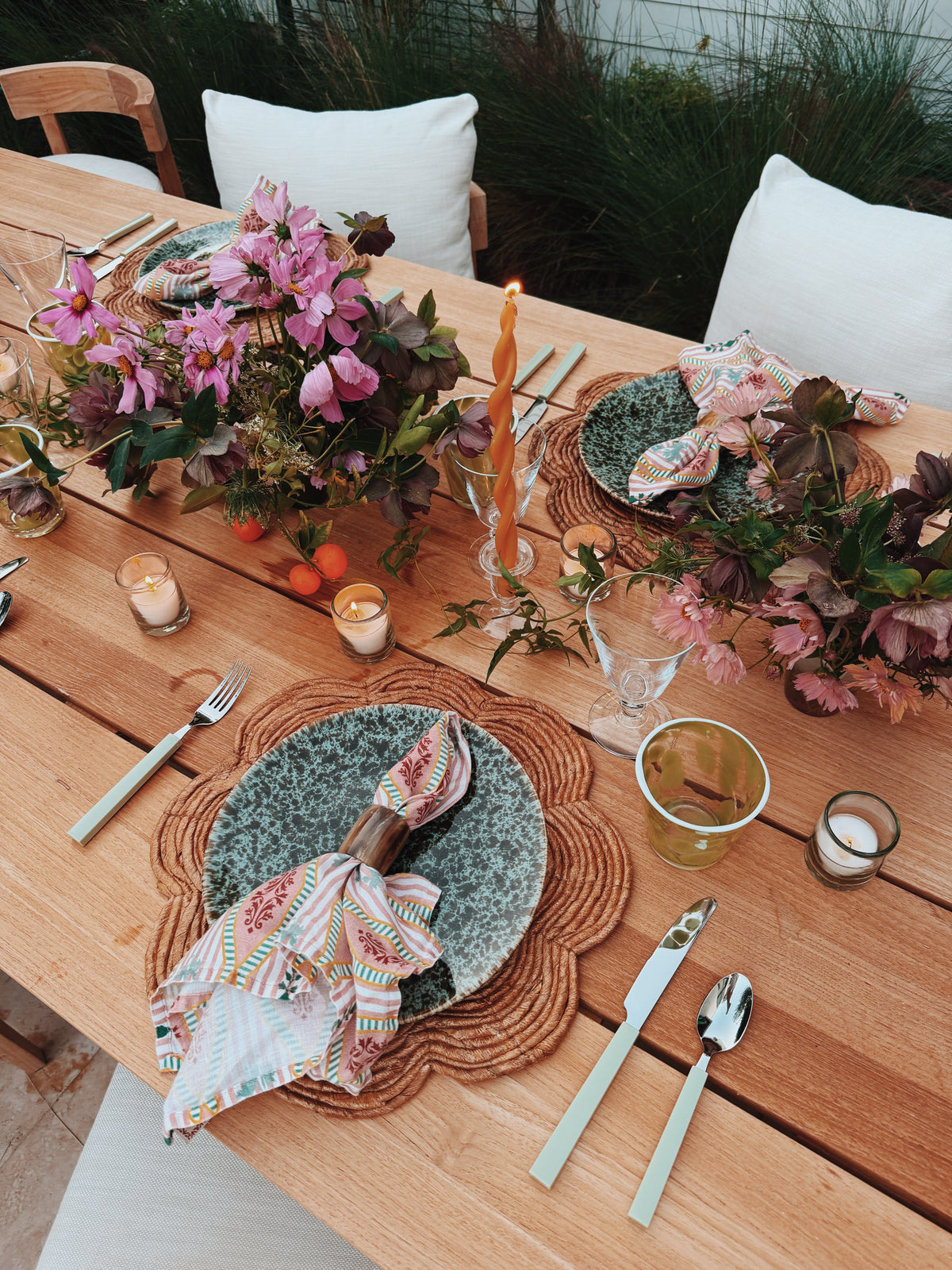 The table laid in daylight with pink flowers, a twisted taper and napkins on the plates