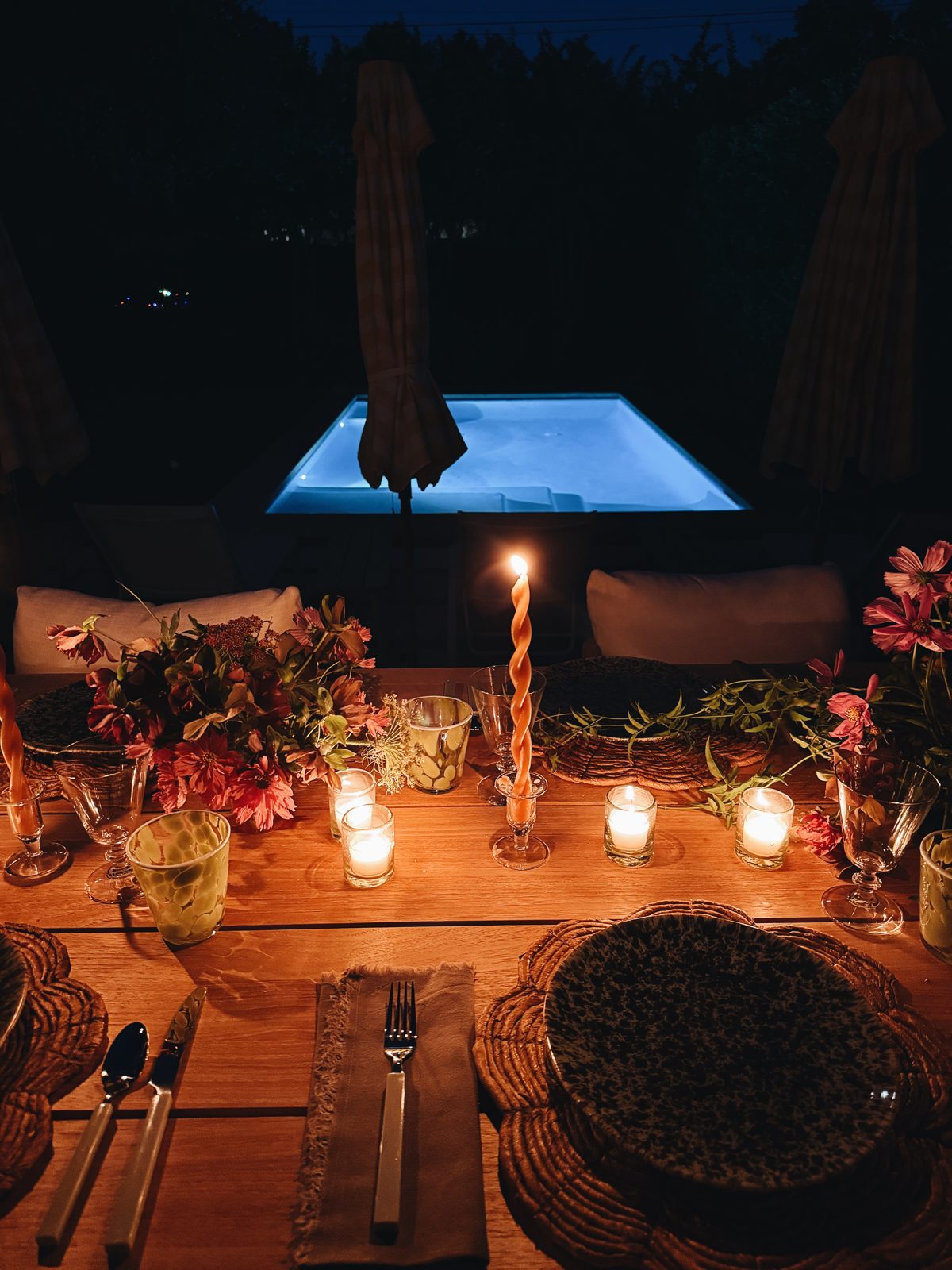 The same table at night, lit by votives and a twisted taper, the pool glowing behind