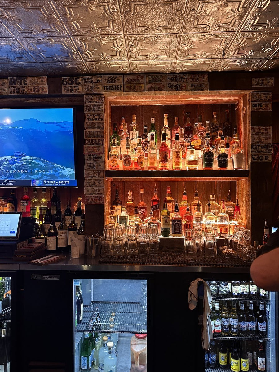 Behind the bar: lit shelves of bottles under a pressed-tin ceiling