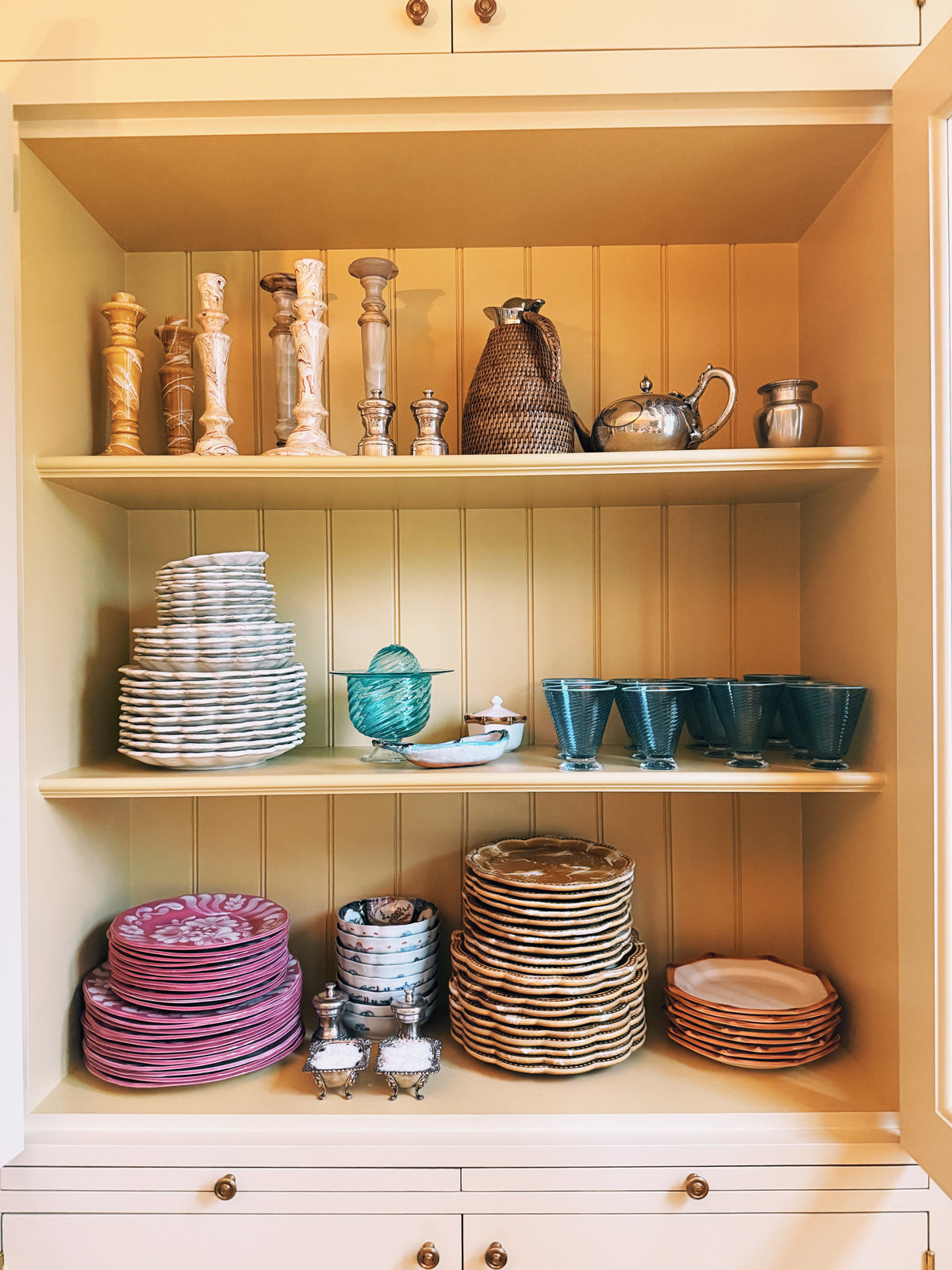 A cupboard of plates stacked in matching sets, pink, white and gold