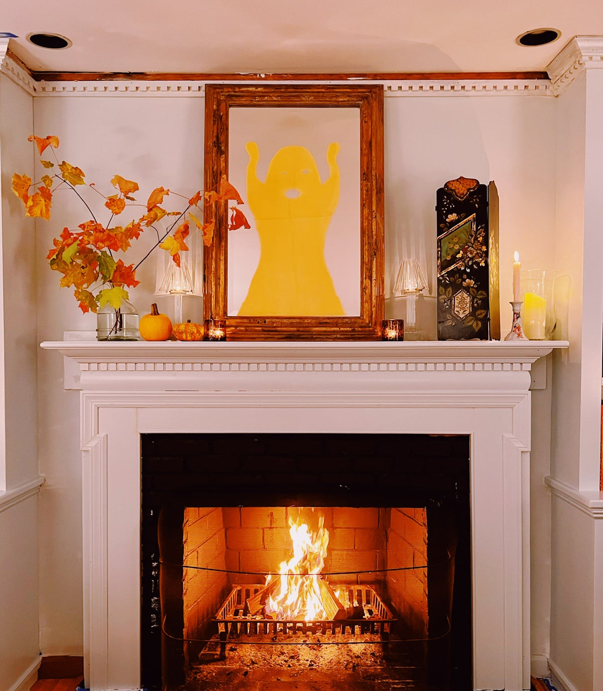 The mantel in autumn: orange leaves, small pumpkins and candles, the fire lit below