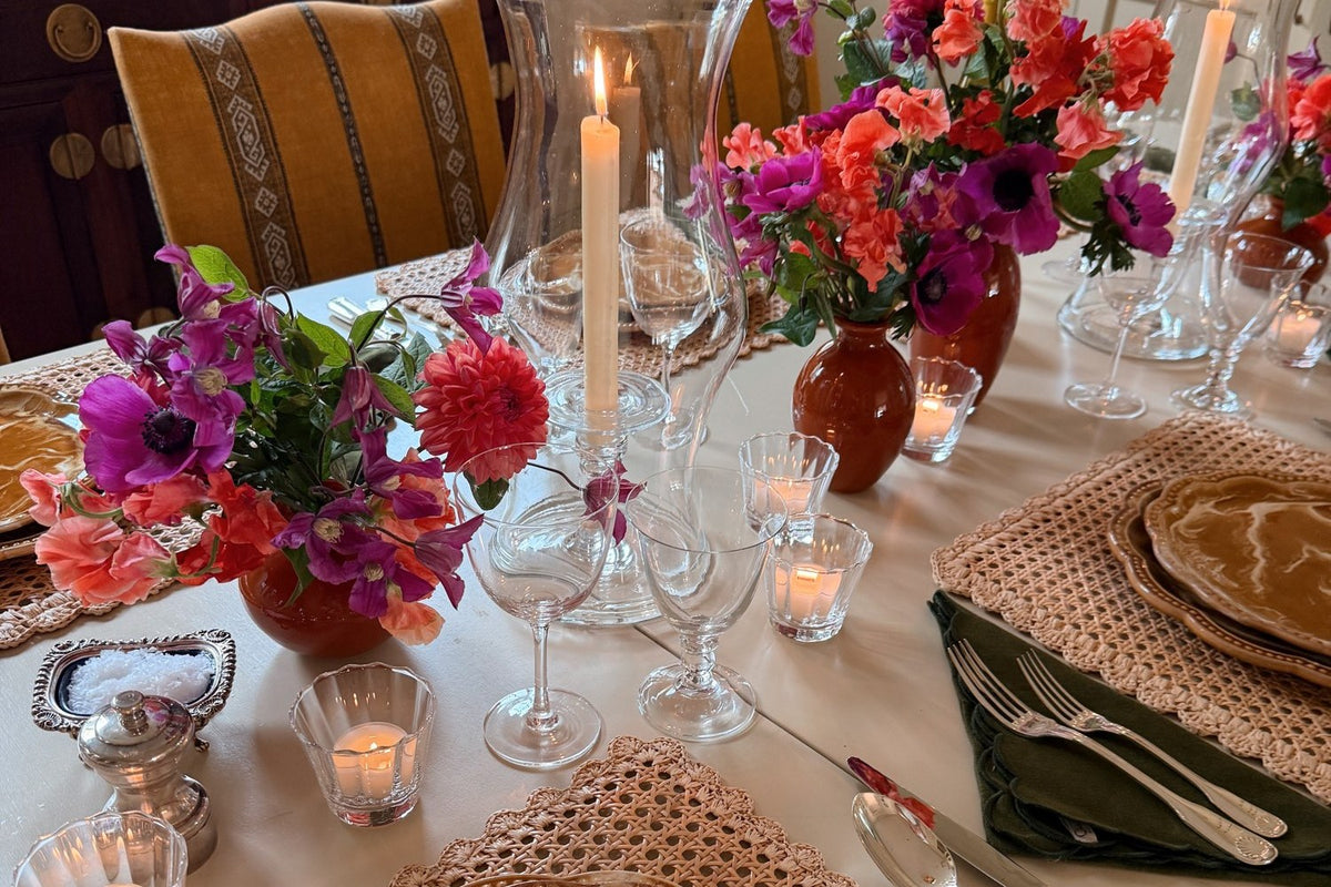 A table laid with marbled plates, woven placemats, green napkins, tall hurricanes and pink and orange flowers
