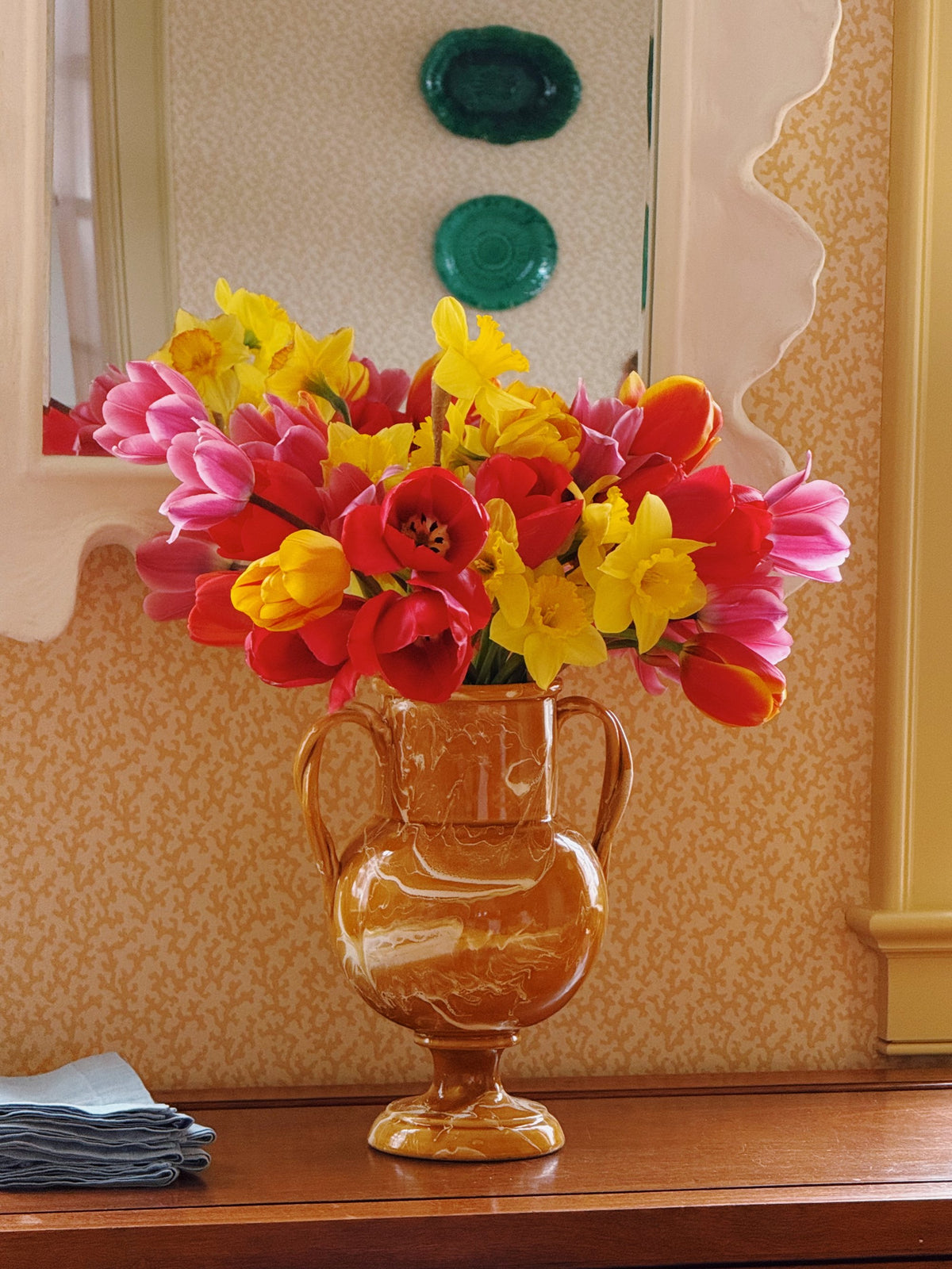 Tulips in a copper urn under a wall of green plates