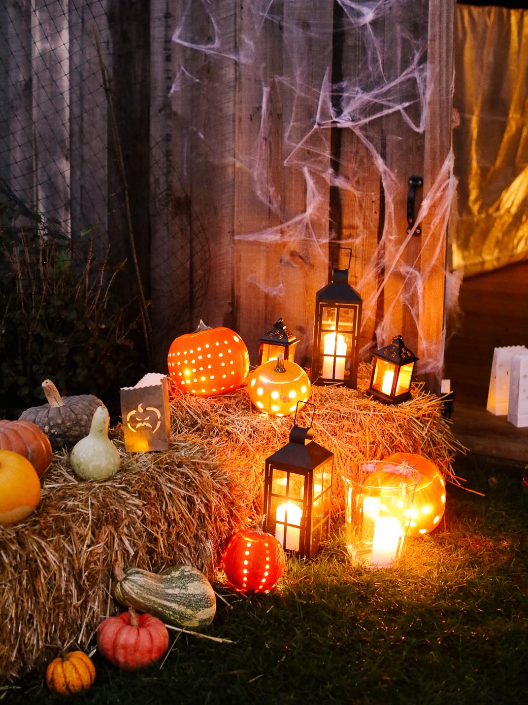 Carved pumpkins, gourds and lanterns on hay bales against the barn wall, hung with cobwebs