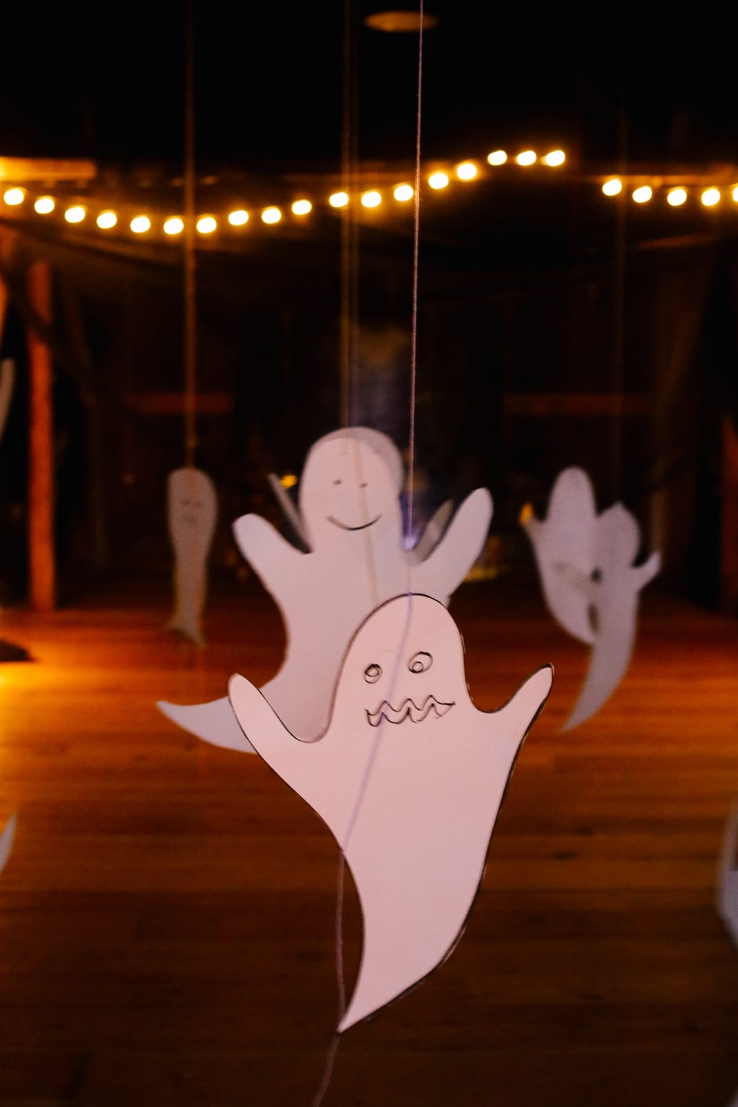 Paper ghosts on strings floating inside the barn under a line of little lights