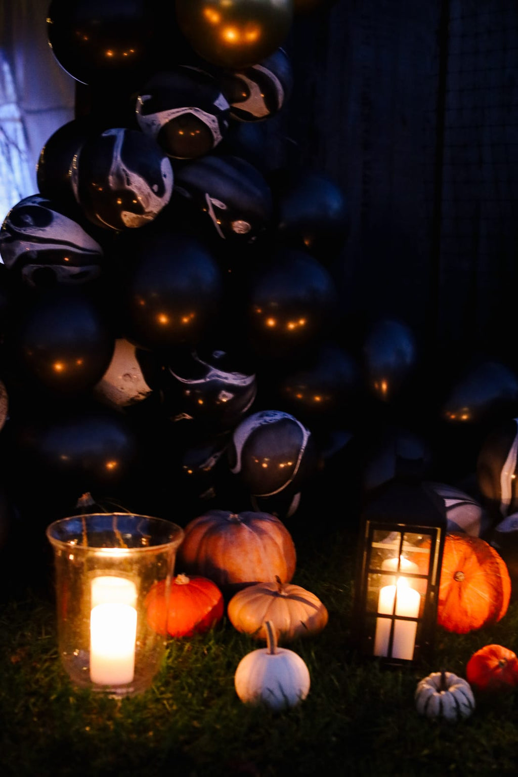Black marbled balloons over a hurricane candle, a lantern and little pumpkins in the grass