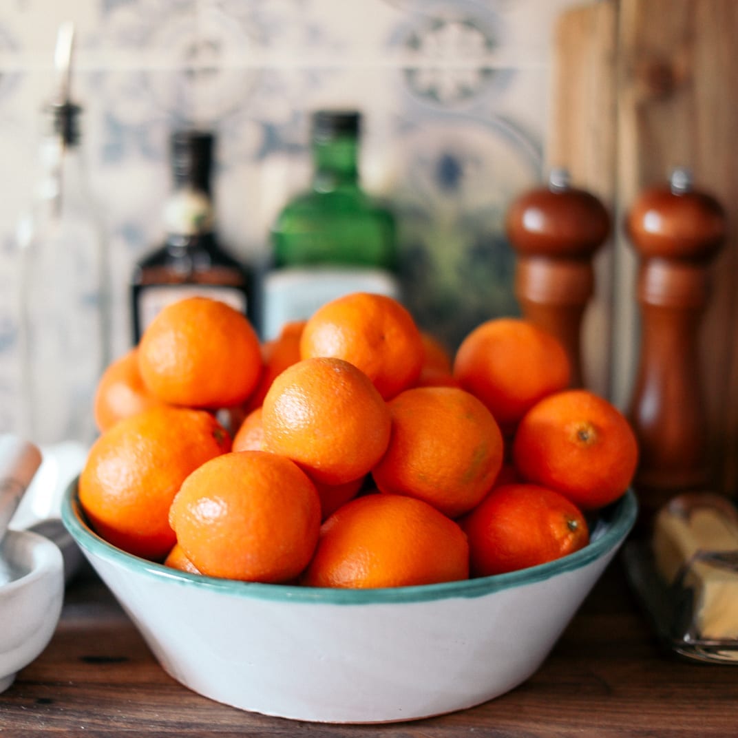A blue and white bowl piled with oranges beside pepper mills and bottles of oil