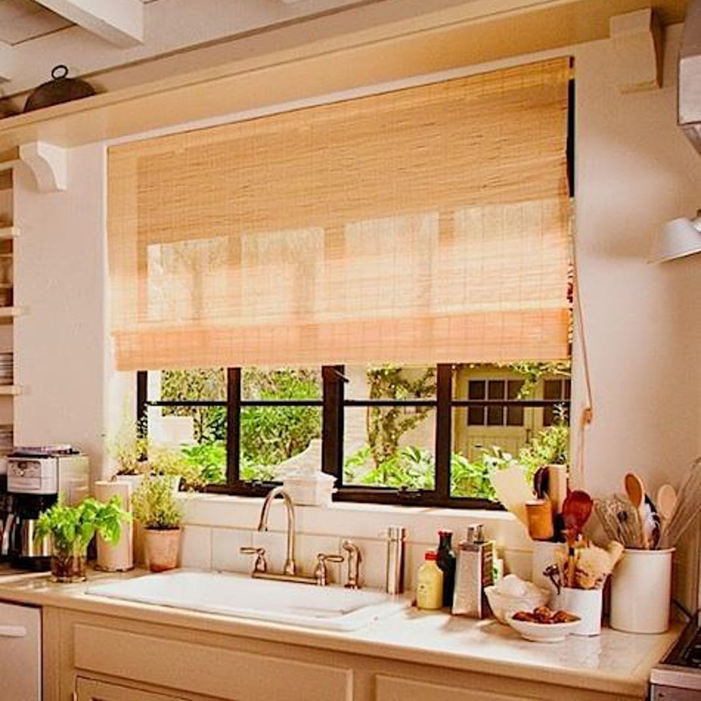 A kitchen sink under a window with a bamboo blind, herbs on the sill and a crock of wooden spoons