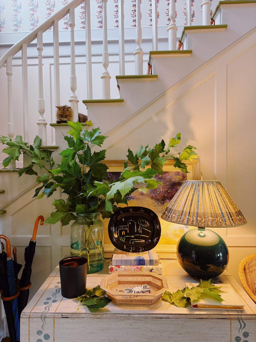 The hall table at the foot of the stairs, a green lamp and a bowl of leaves