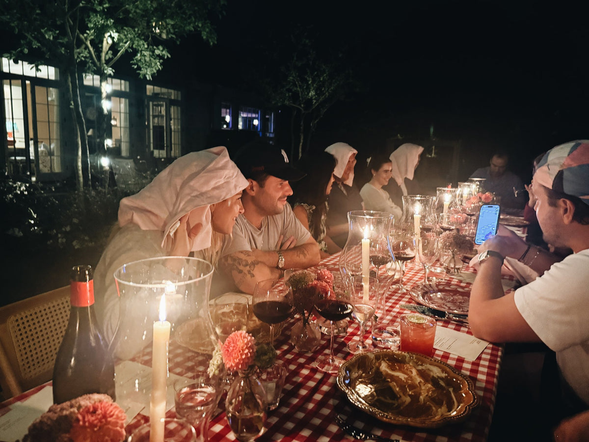 The long table at night, lit by tapers in hurricanes, guests with napkins tied over their heads