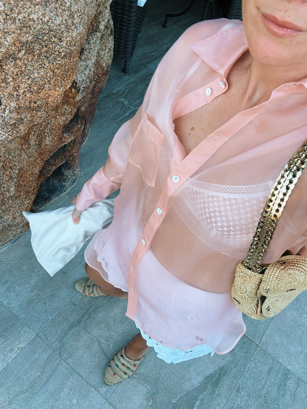 A sheer pink shirt over a white top, a woven gold bag on the shoulder
