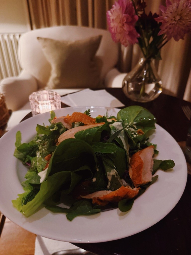A salad at dinner, pink flowers on the table behind
