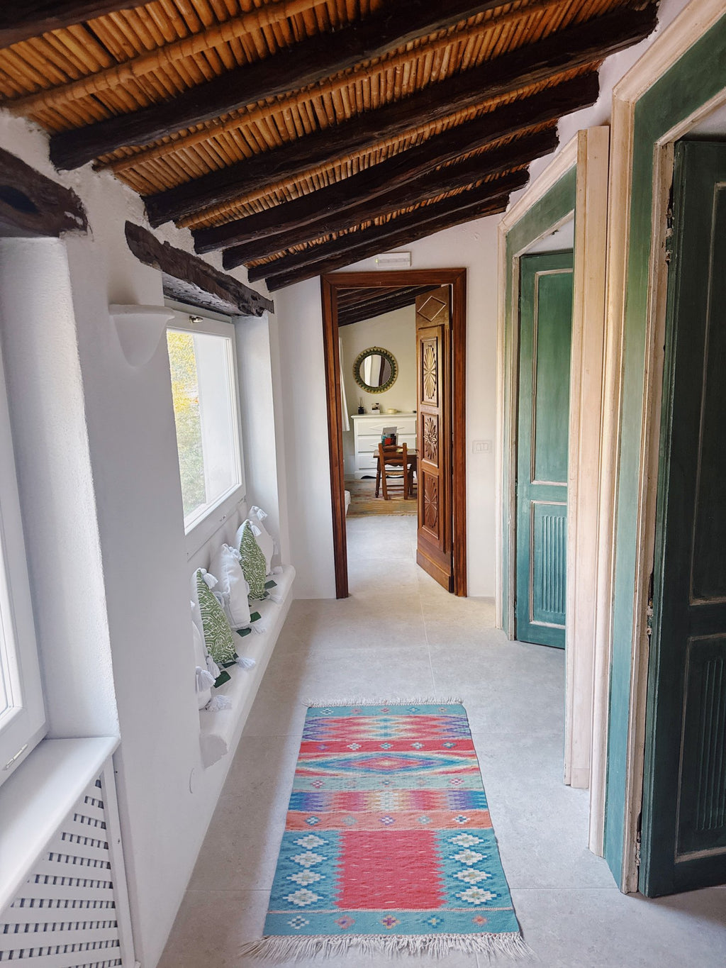 A whitewashed corridor with a beamed ceiling and a striped rug