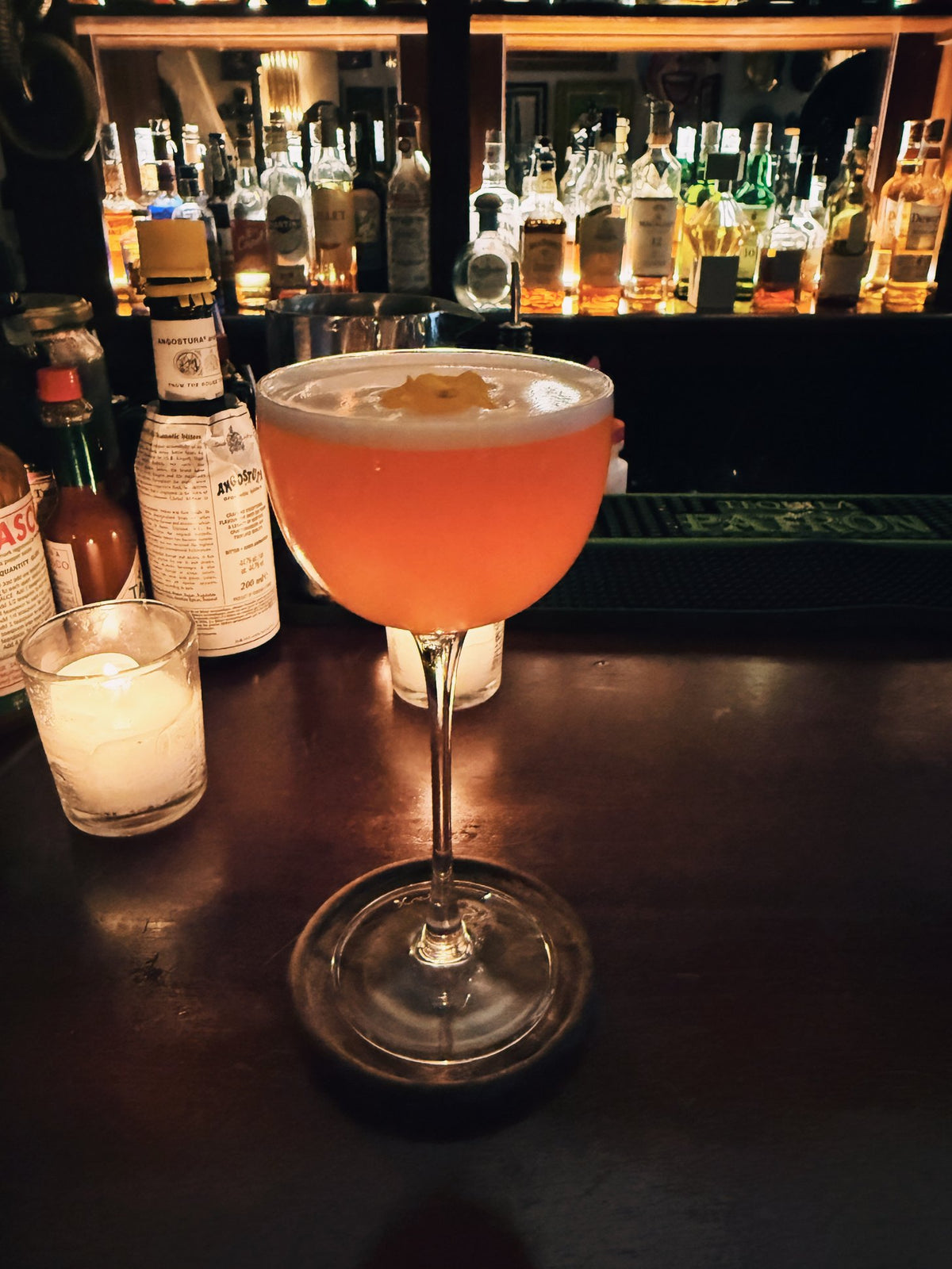 A pink cocktail by candlelight in front of a lit bar
