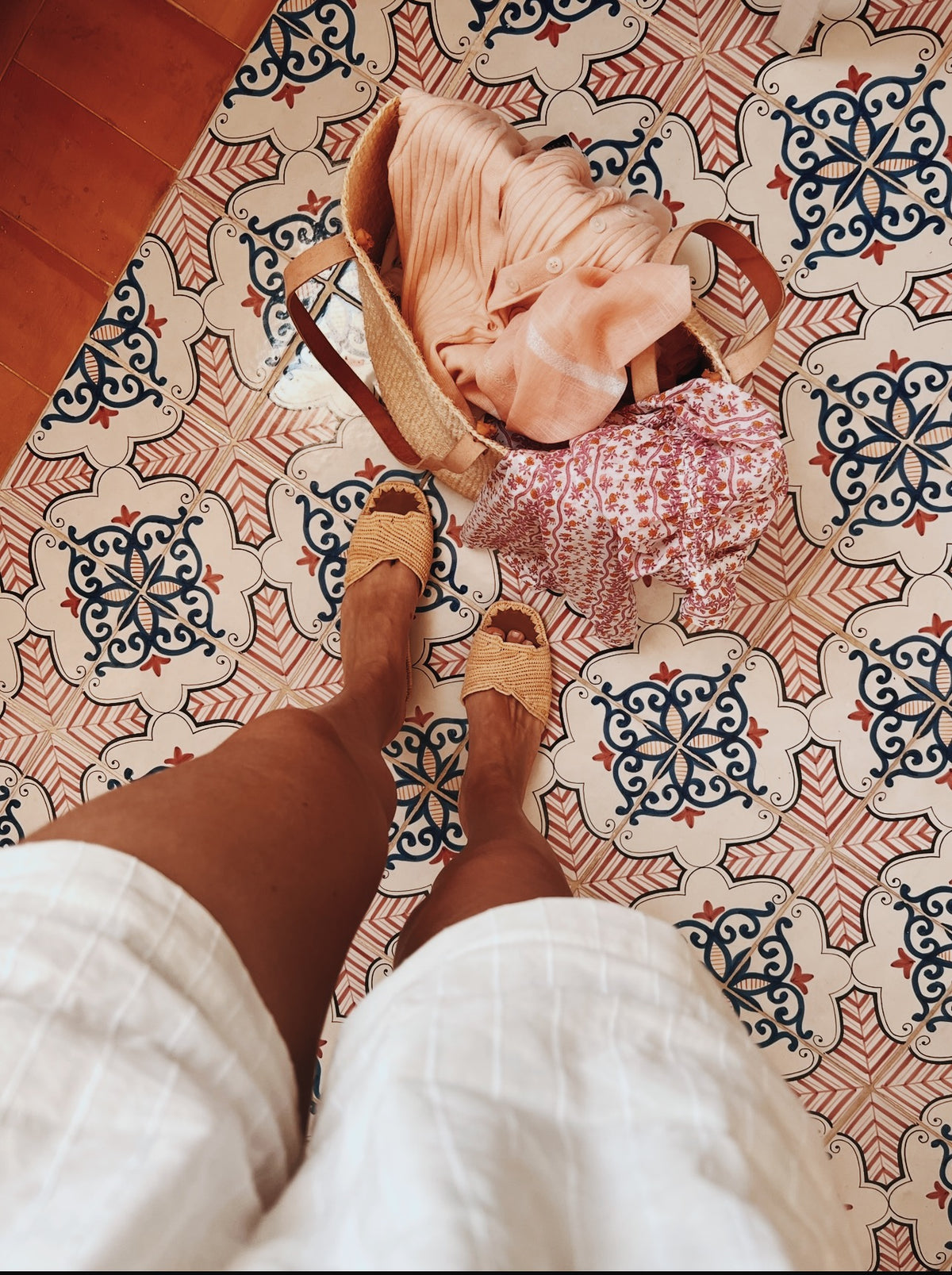 A straw bag and sandals on a painted tile floor