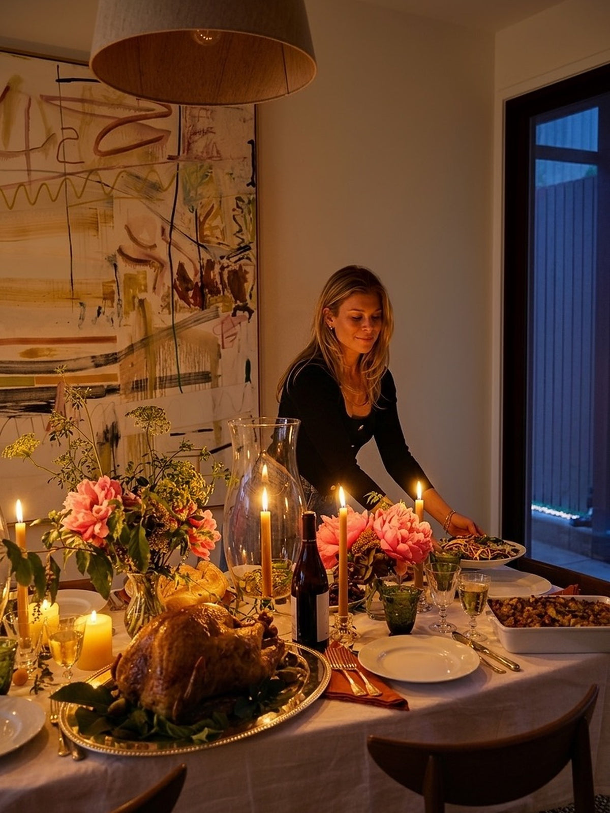 Lucy setting the Thanksgiving table by candlelight, peonies and tapers in front of her