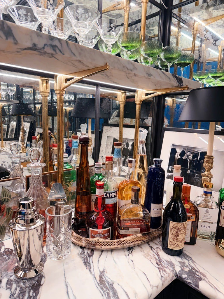 The bar at home: Campari, Grand Marnier and the bottles on a silver tray, a silver shaker, etched coupes and green glasses on the marble shelf above