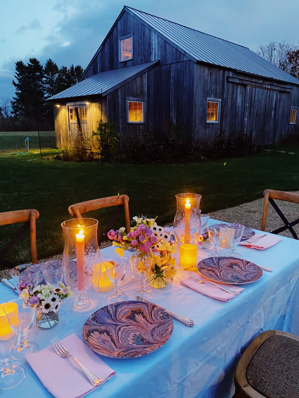A long table set outside a barn at dusk, tapers lit