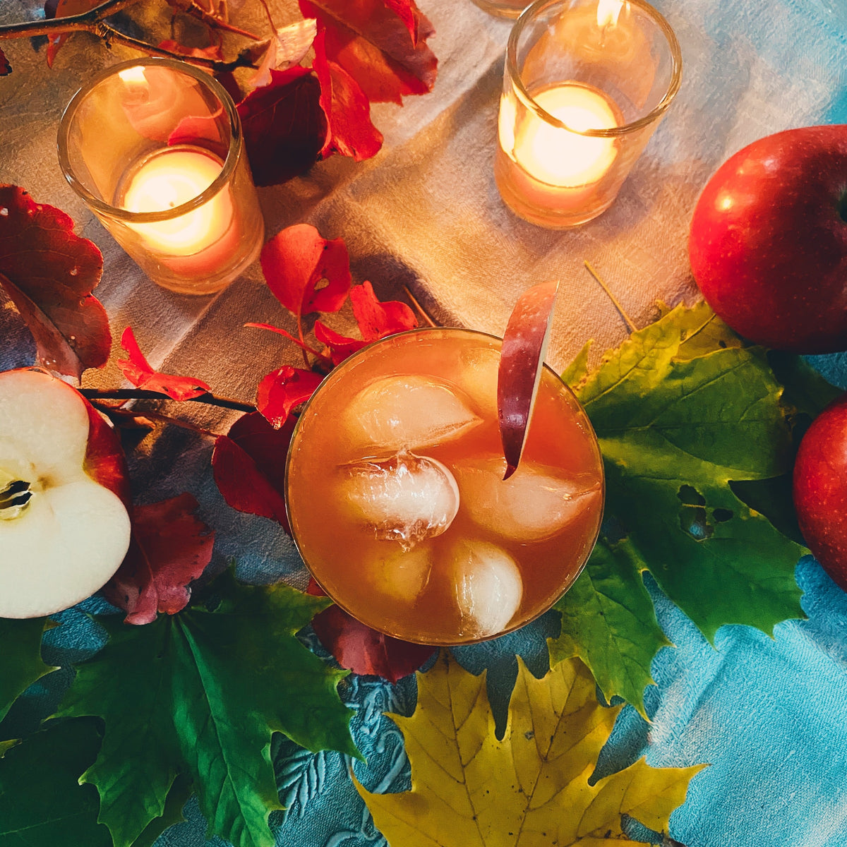 An iced apple cider among autumn leaves, apples and votives