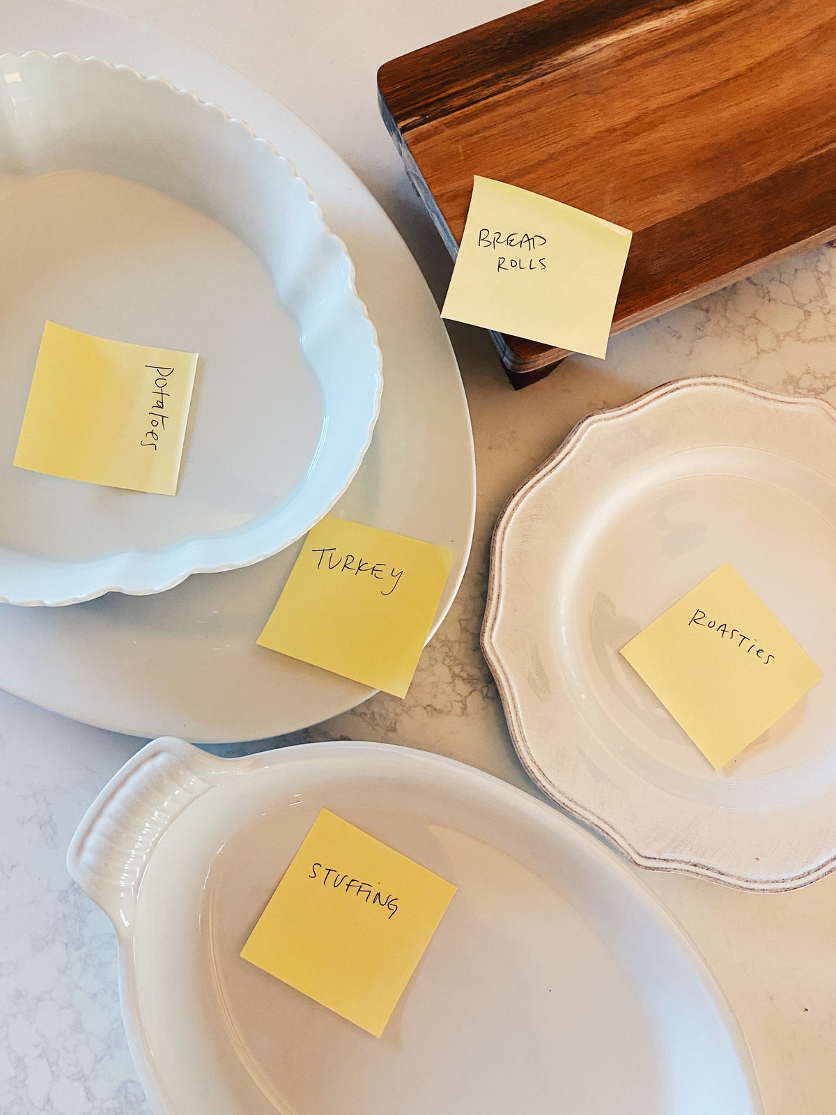 Serving dishes with handwritten sticky notes: potatoes, turkey, stuffing, bread rolls