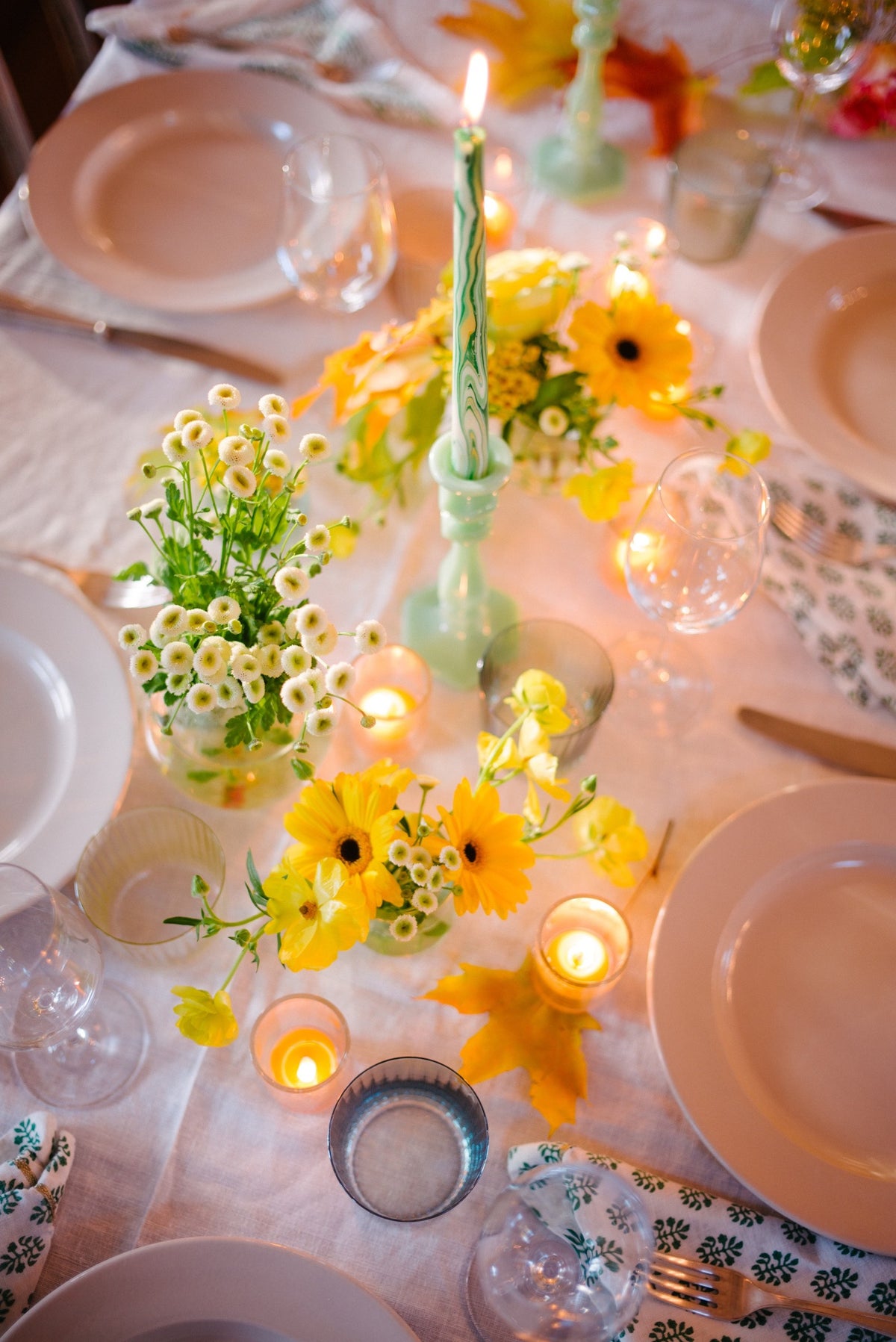 Yellow flowers and a green taper down a white table