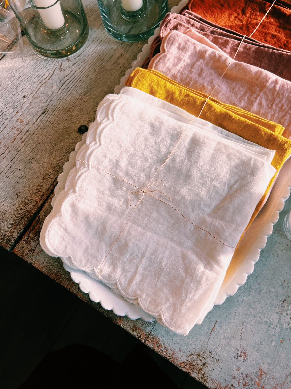 Stacks of linen napkins in white, saffron, blush and rust, tied with string on a scalloped tray
