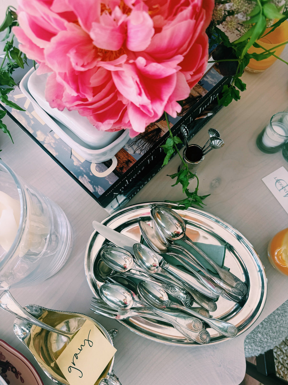 Serving spoons heaped on a silver tray beside a peony and a gravy boat with its name card
