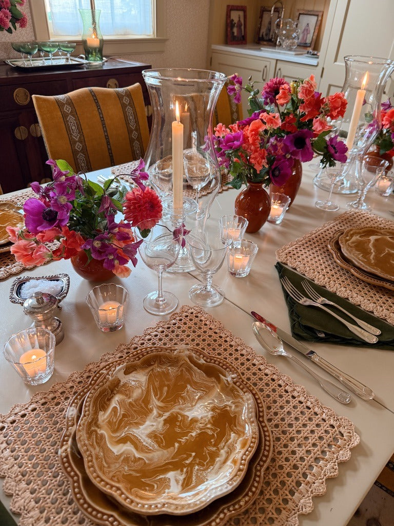 The table set with yellow marbled plates on cane placemats, pink flowers and candles