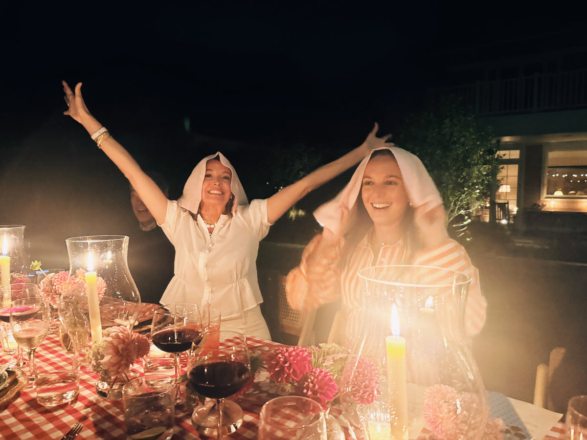 Friends at a candlelit table late at night, arms in the air