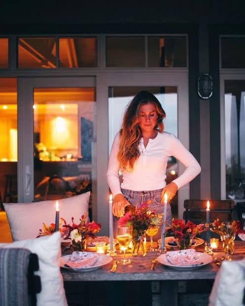 Lucy lighting the table at dusk, tapers and votives among low red flowers