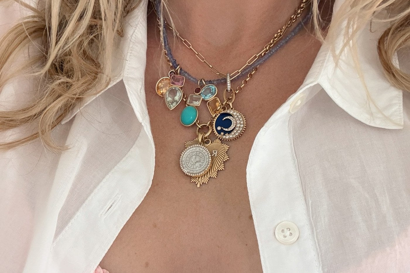 Layered gold necklaces and charms over a white shirt